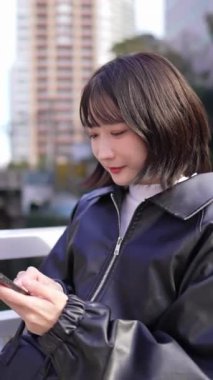 20 'li yaşlarda genç bir Japon kadının Gotanda İstasyonu, Shinagawa-ku, Tokyo' da kışın durup akıllı telefonunu kullanmasının dikey videosu.