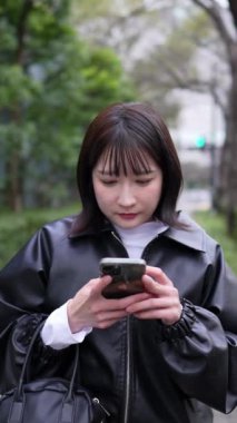 20 'li yaşlarda genç bir Japon kadının Gotanda İstasyonu, Shinagawa-ku, Tokyo' da kışın durup akıllı telefonunu kullanmasının dikey videosu.