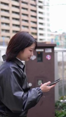 Japon bir kadının kışın akıllı telefonunu kullanırken Gotanda İstasyonu, Shinagawa-ku, Tokyo 'da dolaştığını gösteren dikey yavaş çekim videosu.