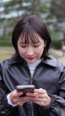 Japon bir kadının kışın Shinagawa-ku, Tokyo 'daki Gotanda İstasyonu yakınlarındaki bir parkta oturduğu dikey yavaş çekim videosu.