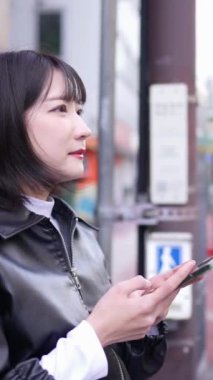 Japon bir kadının 20 'li yaşlarda Gotanda İstasyonu, Shinagawa-ku, Tokyo' da kışın akıllı telefon kullanmasını gösteren dikey yavaş çekim videosu.