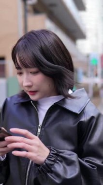 Japon bir kadının 20 'li yaşlarda Gotanda İstasyonu, Shinagawa-ku, Tokyo' da kışın akıllı telefon kullanmasını gösteren dikey yavaş çekim videosu.