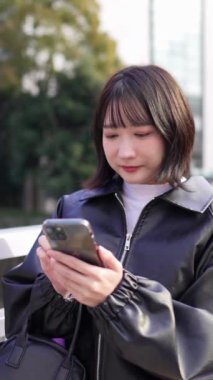 Japon bir kadının 20 'li yaşlarda Gotanda İstasyonu, Shinagawa-ku, Tokyo' da kışın akıllı telefon kullanmasını gösteren dikey yavaş çekim videosu.