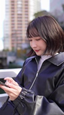 Japon bir kadının 20 'li yaşlarda Gotanda İstasyonu, Shinagawa-ku, Tokyo' da kışın akıllı telefon kullanmasını gösteren dikey yavaş çekim videosu.