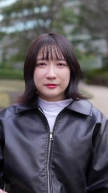 20 'li yaşlarda Japon bir kadının kışın Shinagawa-ku, Tokyo' daki Gotanda İstasyonu yakınlarındaki bir parkta konuşmasının dikey yavaş çekim videosu. 