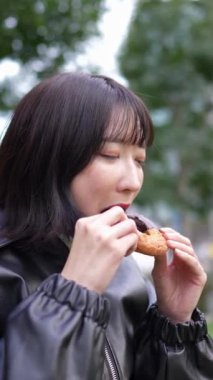 Japon bir kadının kışın, Gotanda İstasyonu, Shinagawa-ku, Tokyo yakınlarındaki bir parkta oturup çörek yerken çekilmiş dikey yavaş çekim videosu. 