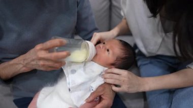 70 'li yaşlarda bir büyükanne ve 30' lu yaşlarında bir anne beyaz kostümlü sekiz günlük Tayvanlı bir bebeğe süt veriyor.