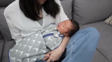 30 'larında Tayvanlı bir anne, elinde 8 günlük beyaz kostümlü bir bebekle kanepede oturuyor.. 