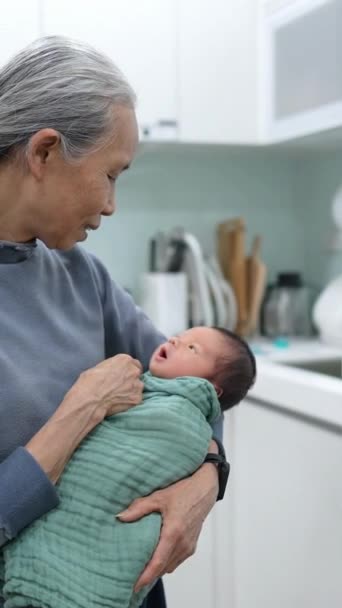 一个70多岁的台湾祖母抱着一个8天大的婴儿 裹在厨房的绿色包裹里的垂直录像 — 图库视频影像