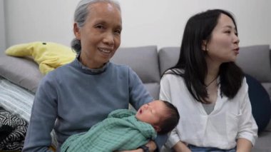 70 'li yaşlarda Tayvanlı bir büyükannenin, 30' lu yaşlarda bir annenin elinde 8 günlük beyaz kostümlü bir bebekle kanepede oturmasının yavaş çekim videosu. 
