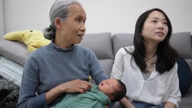 70 'li yaşlarda Tayvanlı bir büyükannenin, 30' lu yaşlarda bir annenin elinde 8 günlük beyaz kostümlü bir bebekle kanepede oturmasının yavaş çekim videosu. 