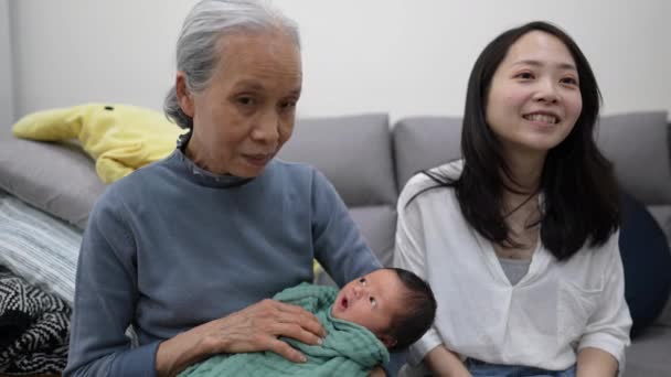 一位70多岁的台湾祖母和一位30多岁的母亲坐在沙发上抱着一位身穿白衣的8天大婴儿的慢镜头 — 图库视频影像