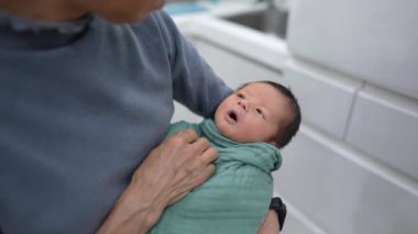 70 'li yaşlarda Tayvanlı bir büyükannenin 8 günlük bir bebeği yeşil bir paketle mutfağa sardığı yavaş çekim videosu.