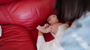 20 'li yaşlarda Tayvanlı bir anne, bir aylık bebeğini kırmızı bir kanepede değiştiriyor..