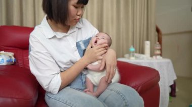 20 'li yaşlarda Tayvanlı bir anne, bir aylık bebeğini kırmızı bir kanepede değiştiriyor..
