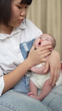 20 'li yaşlarda Tayvanlı bir annenin kırmızı bir kanepede geğirerek 1 aylık bebeğini doğuruşunun dikey videosu..