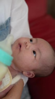 20 'li yaşlardaki Tayvanlı bir annenin 1 aylık bir kızın bebeğine evde kırmızı bir kanepede süt verirken çekilmiş dikey videosu.