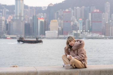 20 'li yaşlarda genç bir kadın akşamları Hong Kong' daki Kowloon Adası 'ndaki deniz manzaralı bir parkta yerel balık köfteleri yiyor.