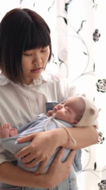 20 'li yaşlarda Tayvanlı bir annenin 1 aylık bir kızı iç mekan perdesinin önünde becerdiği dikey yavaş çekim videosu.