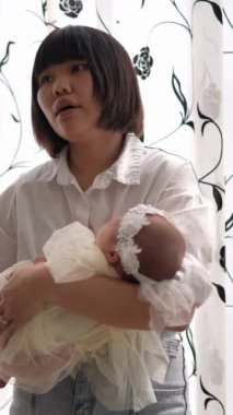 20 'li yaşlarda Tayvanlı bir annenin 1 aylık bir kızı iç mekan perdesinin önünde becerdiği dikey yavaş çekim videosu.