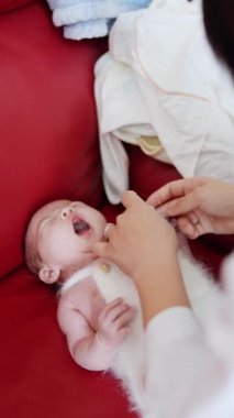 20 'li yaşlarda Tayvanlı bir annenin kırmızı bir kanepede 1 aylık bebeğini değiştirdiği dikey yavaş çekim videosu.
