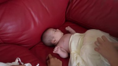 20 'li yaşlarda Tayvanlı bir annenin kırmızı bir kanepede 1 aylık bebeğini değiştirdiği yavaş çekim videosu.