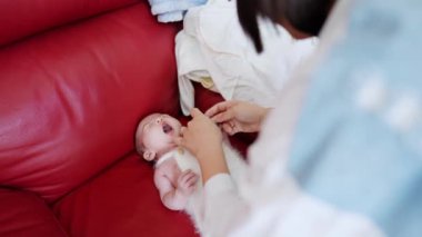 20 'li yaşlarda Tayvanlı bir annenin kırmızı bir kanepede 1 aylık bebeğini değiştirdiği yavaş çekim videosu.