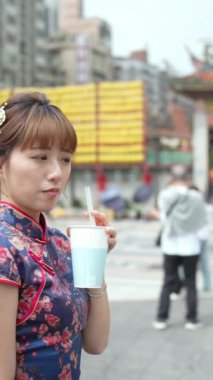 Tayvan 'da Wanhua Bölgesi' nde geleneksel Çin elbisesi giyen 20 'li yaşlarda Tayvan' lı bir kadının Longshan Tapınağı yakınlarında tapyoka sütlü çay içerken dolaştığı dikey bir video..
