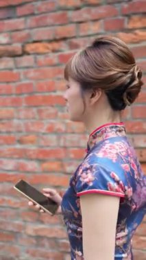 Tayvan 'ın Tayvan şehrinde Wanhua bölgesinde, geleneksel Çin elbisesi giyen, 20' li yaşlarda Tayvanlı bir kadının tuğla bir duvarın önünde yürüdüğü dikey bir video.