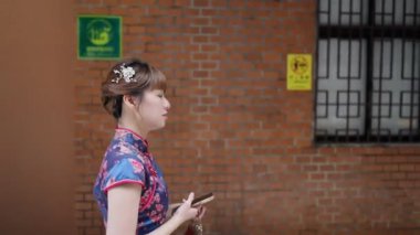 Tayvan 'ın Tayvan şehrinde Wanhua bölgesinde akıllı telefonunu kullanırken geleneksel bir Çin elbisesi giyen 20' li yaşlarda Tayvanlı bir kadın yürüyor.