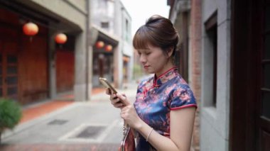 Tayvan 'ın Taipei şehrinin tarihi Bopiliao Tarihi Bloğu' nda, 20 'li yaşlarda, geleneksel mavi bir elbise giyen bir Tayvanlı kadın ayakta duruyor ve akıllı telefon kullanıyor..
