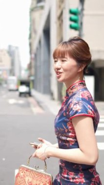 Tayvan, Tayvan 'da Wanhua bölgesinde geleneksel Çin elbisesi giyen 20' li yaşlarda bir Tayvanlı kadının yaya geçidinde akıllı bir telefonla yürüdüğü dikey yavaş çekim videosu.