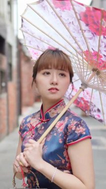 Bu yavaş çekimde, geleneksel mavi Cheongsam 'lı genç bir Tayvanlı kadın Bopiliao Tarihi Blok, Taipei' de duruyor. Elinde süslü bir şemsiye tutarak zarafet ve kültürel zenginliği temsil ediyor.