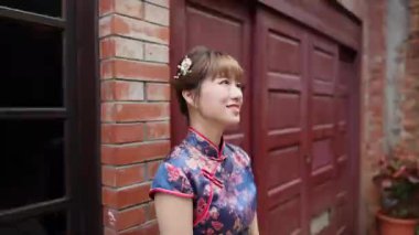 20 'li yaşlarda gülümseyen Tayvanlı bir kadın geleneksel mavi bir Cheongsam elbisesi giymiş tarihi Bopiliao Tarihi Bloğu' nun arka sokağında duruyor..