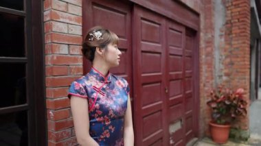 20 'li yaşlarda gülümseyen Tayvanlı bir kadın geleneksel mavi bir Cheongsam elbisesi giymiş tarihi Bopiliao Tarihi Bloğu' nun arka sokağında duruyor..