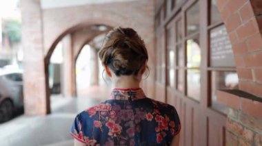 Tayvanlı genç bir kadın mavi çiçekli Cheongsam elbisesiyle Bopiliao Old Street, Wanhua District, Taipei City 'de kemerli sütunlarda yürüyor. Yavaş çekim