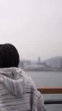Genç bir Hong Kong 'lu kadın, arka planda şehrin ufuk çizgisi ile derin derin deniz kenarında duruyor. North Point' teki East Coast Park Karakolu 'nun sakin ama hareketli bir çevresini gözler önüne seriyor..