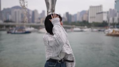 Hong Kong 'un Causeway Körfezi' ndeki genç bir kadın limana bakan korkuluklara yaslanıyor. O sıradan bir kazak ve kot etek giyer. Yavaş çekim videosu onun şehir manzarasına karşı derin düşüncelere daldığı anı yakalıyor.. 