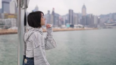 Hong Kong 'un Causeway Körfezi' ndeki genç bir kadın limana bakan korkuluklara yaslanıyor. O sıradan bir kazak ve kot etek giyer. Yavaş çekim videosu onun şehir manzarasına karşı derin düşüncelere daldığı anı yakalıyor.. 