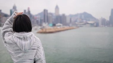 Hong Kong 'un Causeway Körfezi' nde genç bir kadın denizin kenarında dikilip, düşünceli bir şekilde şehrin ufuk çizgisine bakıyor..