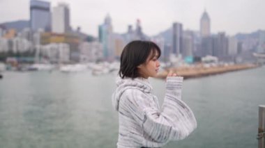Hong Kong 'un Causeway Körfezi' nde genç bir kadın denizin kenarında dikilip, düşünceli bir şekilde şehrin ufuk çizgisine bakıyor..