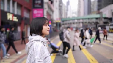 Causeway Bay Hong Kong 'da yoğun bir yaya geçidinde yürüyen genç bir kadın kalabalık bir arka planda göze çarpıyor. Yavaş çekim etkisi, kentin ortasında onun dingin varlığını yakalıyor.