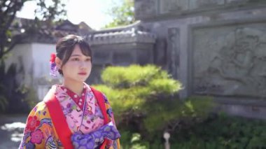Geleneksel Ryusou giyimli yirmili yaşlarda genç bir kadın Okinawa 'daki güzel bir Çin bahçesinde zarifçe geziniyor. Çevrenin kültürel karışımını ve dingin güzelliğini vurguluyor..