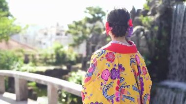 Geleneksel Ryusou giyimli yirmili yaşlarda genç bir kadın Okinawa 'daki güzel bir Çin bahçesinde zarifçe geziniyor. Çevrenin kültürel karışımını ve dingin güzelliğini vurguluyor..