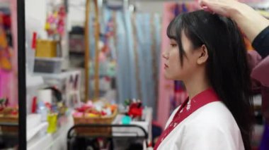 Geleneksel Ryusou giyen yirmili yaşlarda genç bir kadın saçını ve makyajını Okinawa 'da içeride yaptırıyor. Sahne, geleneksel kültürün ayrıntılı işleyişini ve zarafetini yansıtıyor.