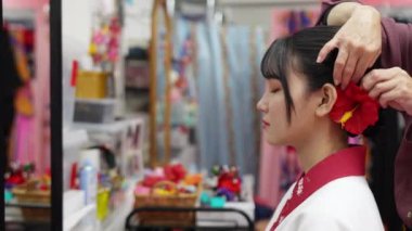 Geleneksel Ryusou giyen yirmili yaşlarda genç bir kadın saçını ve makyajını Okinawa 'da içeride yaptırıyor. Sahne, geleneksel kültürün ayrıntılı işleyişini ve zarafetini yansıtıyor.
