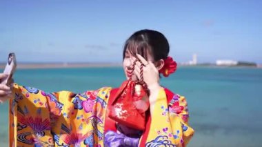 Geleneksel Ryusou giyimli yirmili yaşlarda genç bir kadın, Okinawa 'da güzel bir sahil kenarında duruyor. Okinawa' nın kültürel zarafetini ve doğal ihtişamını vurguluyor..