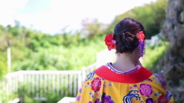 Geleneksel Ryusou giyen yirmili yaşlarında genç bir kadın Okinawa 'da açık havada yürüyor. Giysileri Okinawa geleneklerinin kültürel zarafetini ve tarihsel önemini vurguluyor..