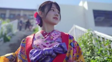 Geleneksel Ryusou giyimli yirmili yaşlarda genç bir kadın Okinawa 'da bir sahil kasabasının merdivenlerinde geziniyor ve mekanın kültürel zarafetini ve manzarasının güzelliğini vurguluyor..