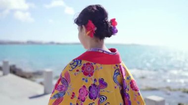 Geleneksel Ryusou giyimli yirmili yaşlarda genç bir kadın Okinawa 'da güzel bir sahil yolunda yürüyor. Okinawa' nın kültürel zarafetini ve doğal ihtişamını vurguluyor..